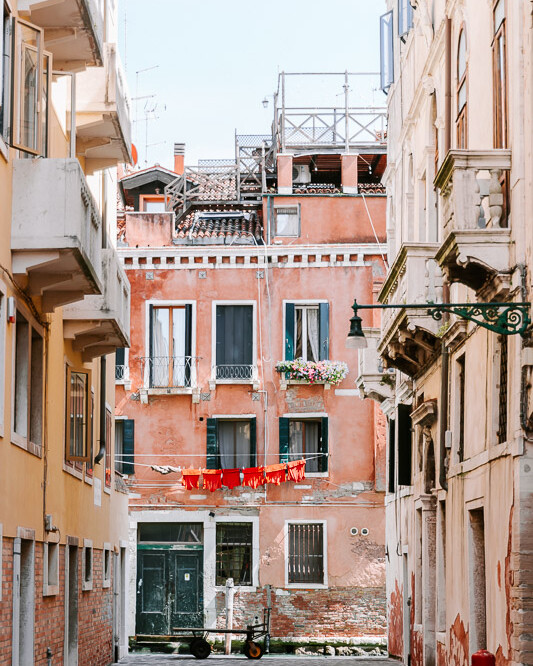 A back street within Venice leading towards a Venice Canal showing the colourful architecture an clothes hanging between the houses