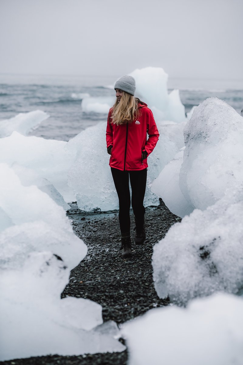 A girl walking amongst icebergs on diamond beach in Iceland during the ring road itinerary