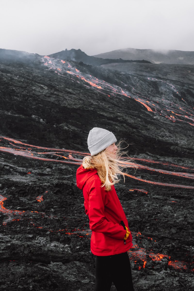 Girl standing in front of the Fagradalsfjall Volcano as lava streams down in Iceland