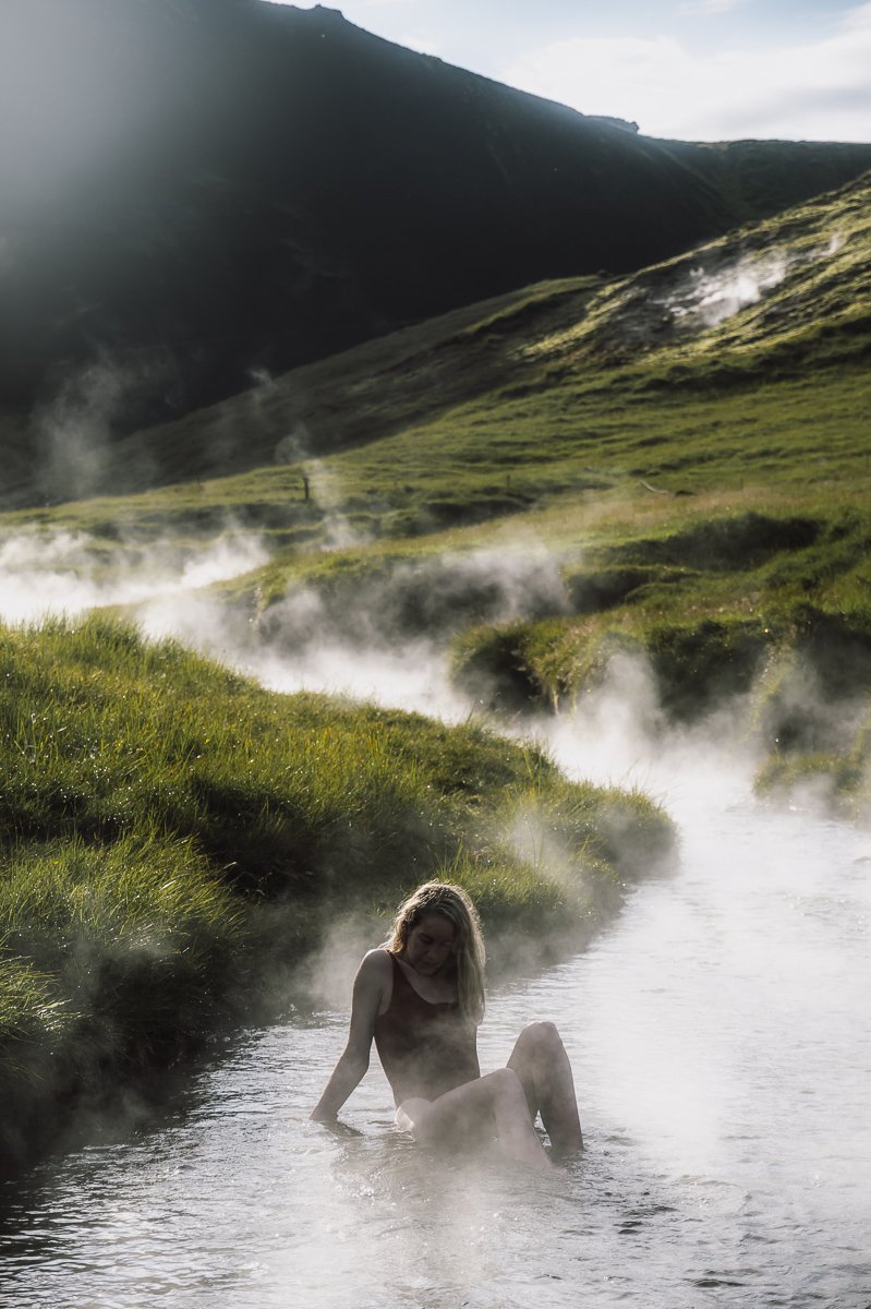 A girl sitting in the Reykjadalur Thermal River with steam rising