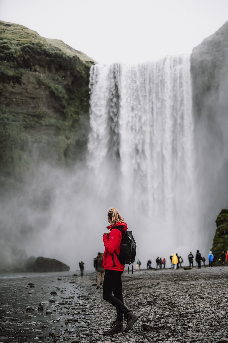 Girl looking up at the Skogafoss waterfall during a ring road iceland itinerary
