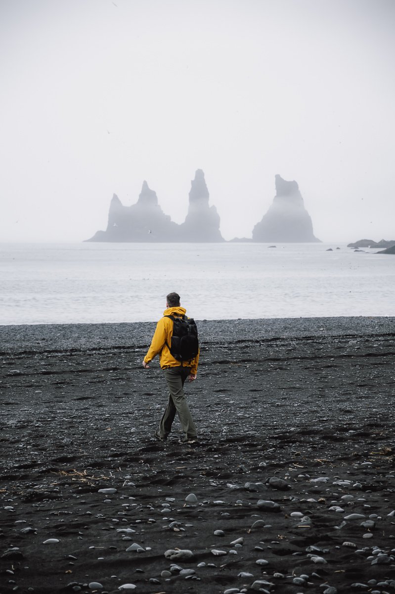 Guy walking on black sand beach in Vik Iceland
